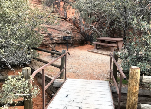 A wooden bridge leads to a picnic area surrounded by rocky terrain and greenery.